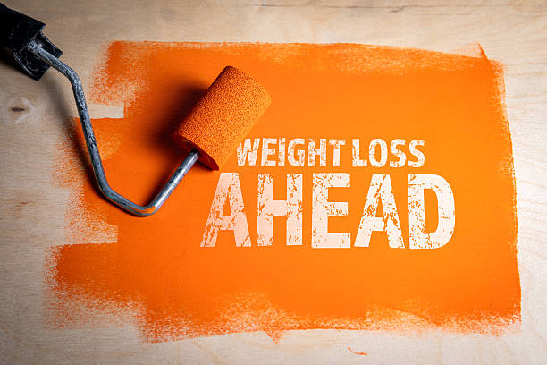 istock Orange painted background with motivational stencil text Weight Loss Ahead and paint roller 2240211677