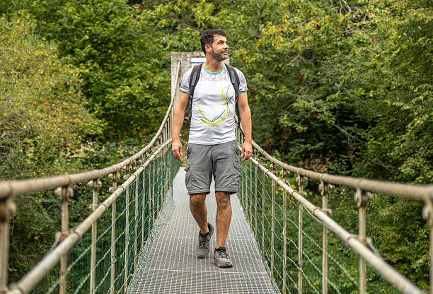 istock Tourist walking on hanging bridge over river in lush forest 2240213192