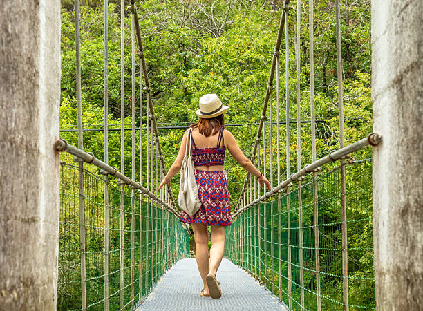 istock Tourist walking on hanging bridge over river in lush forest 2240213211