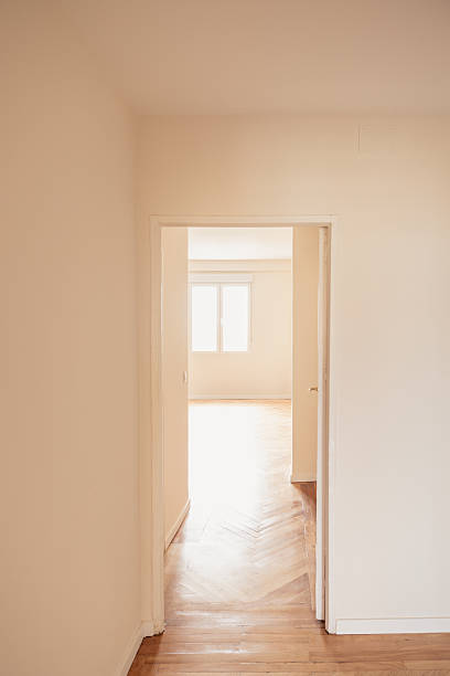 Empty room with wooden floor and bright window, view from the hallway