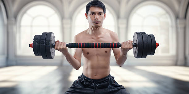 A focused young man lifts heavy dumbbells in a bright fitness studio. His determination and strength showcase his commitment to an active and healthy lifestyle.