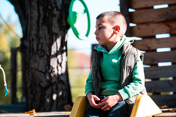 Thoughtful young boy sitting outdoors on a playground structure, looking away and contemplating. Childhood emotions and pensive moments