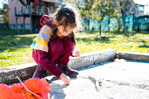 Girl crouching on cracked sidewalk, playing with small objects, showing curiosity and childhood discovery outdoors