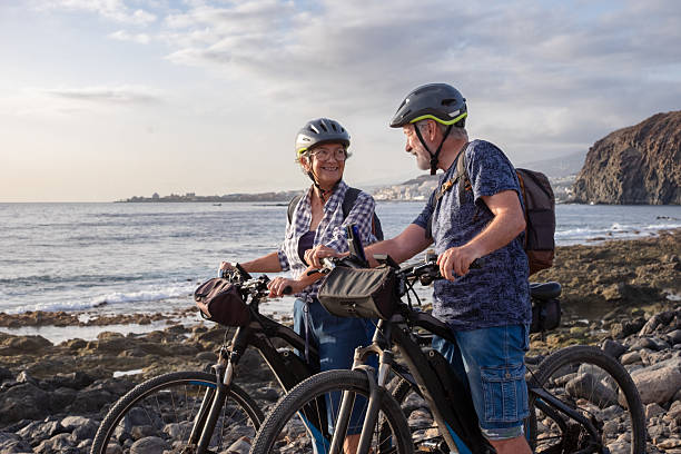 istock Senior active couple riding on the pebble beach with electric bicycles at sunset. Authentic elderly retired life and sustainable mobility concept 2240224703