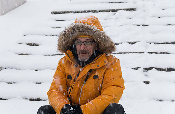 Alone mature man during snowy day in winter. Cheerful man sitting  sitting on snowy steps . Adult man with beard wearing glasses. Winter, snow.
