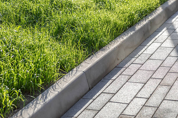 istock Green lawn next to a paved walkway. Landscaped courtyard element with grass and stone walkway. Curb on the border of a rectangular cobblestone walkway and green lawns. Photo 2240225751