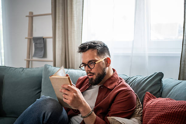 istock Man relaxing at home reading book with glasses 2240226357