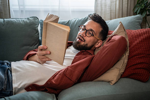 istock Man relaxing on sofa reading book at home 2240226444