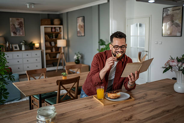 istock Young man enjoying breakfast and reading a book at home 2240232695