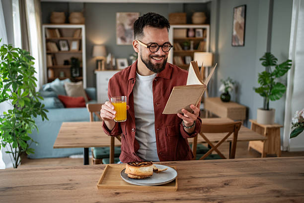 istock Young man enjoying breakfast, reading book at home 2240232707