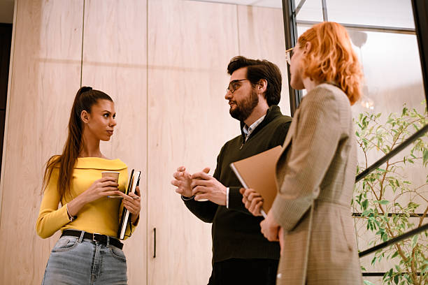 istock Group discussion in modern office space with two women and a man engaged in conversation while holding notebooks 2240234167