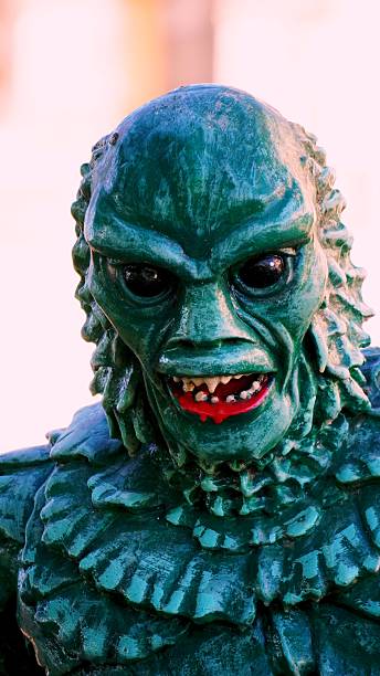 Head shot of a classic horror movie creature costume showing green textured skin, dark eyes, and red mouth with sharp fangs, perfect for a Halloween party