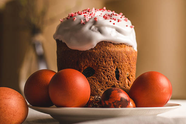 freshly baked easter cake is embellished with white frosting and red sprinkles, surrounded by decorated eggs on table. this setup reflects joyous spring celebration with vibrant colors. close up.