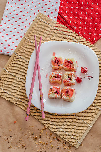 sweet sushi rolls with cherries displayed on white plate. top view. closeup.