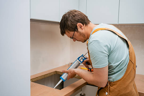 istock Professional plumber sealing kitchen sink edges with silicone, meticulously applying adhesive for watertight installation and preventing potential water damage in contemporary kitchen setting 2240236222