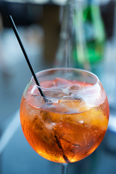 A tall glass filled with a refreshing orange liquid accompanied by ice cubes and topped off with a sleek black straw for easy sipping