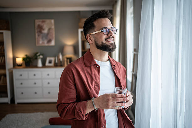 istock Young man drinking water looking out window feeling refreshed 2240238181