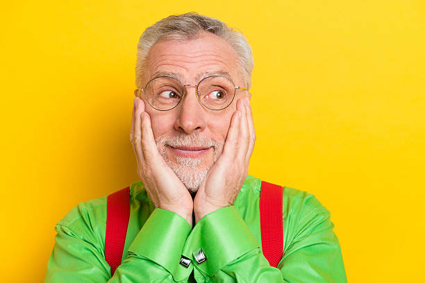 istock Photo portrait old man smiling in glasses looking copyspace amazed touching cheeks isolated bright yellow color background 2240245768