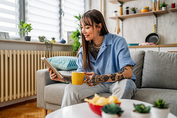 istock Tattooed woman relaxing at home using digital tablet 2240246311