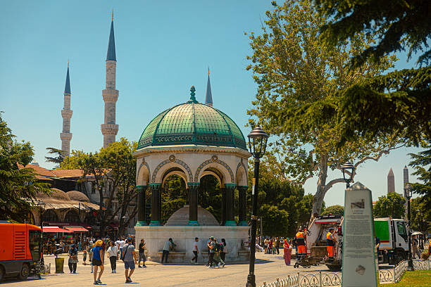 The historic German Fountain in Sultanahmet Square, Istanbul, with the minarets of the Blue Mosque in the background on a bright summer day.