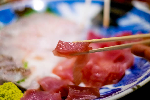 Pick up a piece of tuna sashimi with chopsticks.