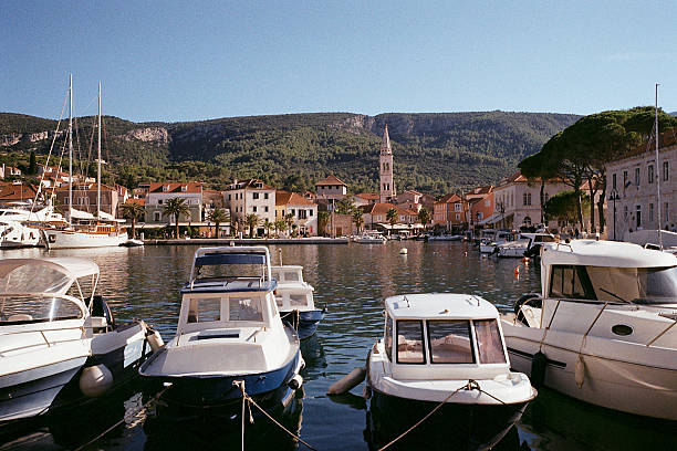 Several small boats moored in a calm harbor with historic Mediterranean buildings and a church tower in the background. Scenic coastal town with mountains and clear sky. Harbor waterfront view.Shot on film camera
