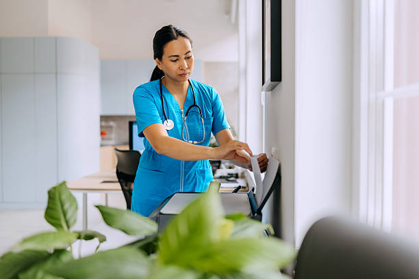 Nurse using printer at hospital office Healthcare professional operating a printer in a hospital office environment. Represents administrative tasks, medical documentation, and daily hospital operations fax stock pictures, royalty-free photos & images