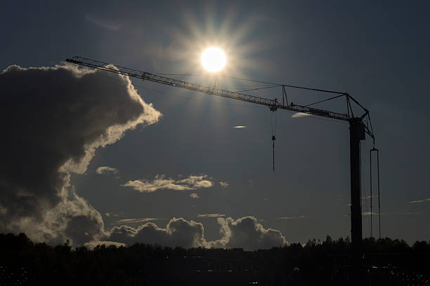 Silhouette of construction crane against the sun or sunset sky.