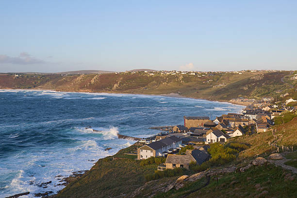 A scenic coastal view featuring a rocky beach with people exploring the shoreline. Waves gently lap at the shore, and cliffs rise in the background, creating a picturesque natural landscape.