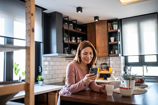 istock Woman using smartphone in kitchen holding coffee 2240263097