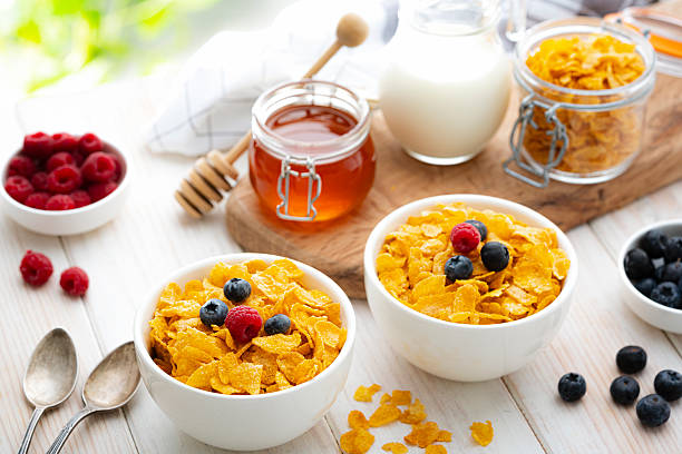 Two bowls filled with corn flakes and berry fruits on white garden table. Breakfast cereal or healthy eating or dieting. Food high in dietary fiber