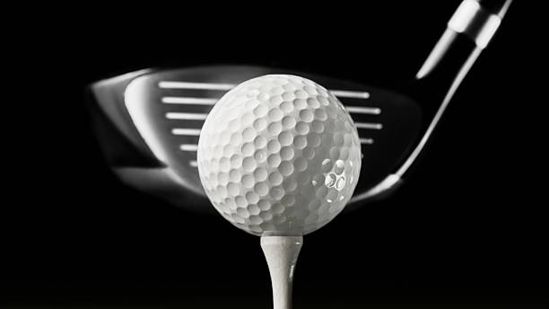 Golf ball on tee with driver club in sharp close-up against black background
