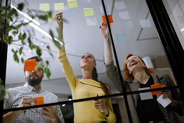istock Team members engaged in brainstorming session with sticky notes on glass window, focusing on collaboration and idea generation in a modern office 2240272587