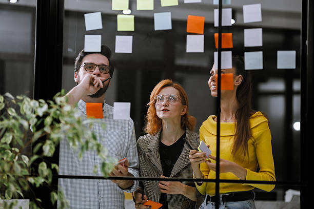 istock Team members collaborating in a modern office space by a glass wall covered with colorful sticky notes during a brainstorming session in the afternoon 2240272601