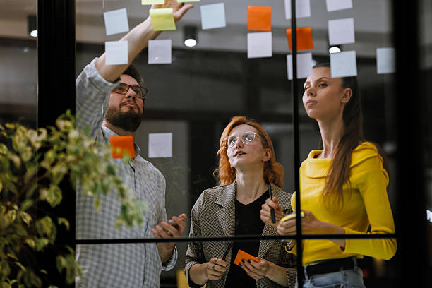 istock Group brainstorming session in an office with sticky notes on glass wall during a creative meeting 2240272613