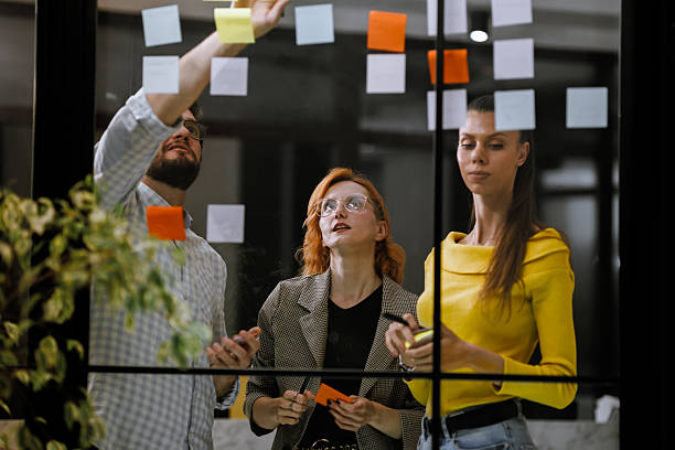 istock Group brainstorming session in a modern office with colorful sticky notes on glass wall during afternoon hours 2240272623