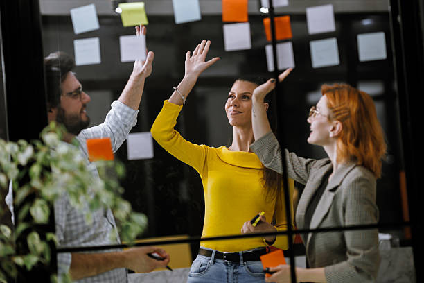 istock Team brainstorming session in a bright office with colorful sticky notes on a glass wall, showcasing collaboration and creativity during a morning meeting 2240272633