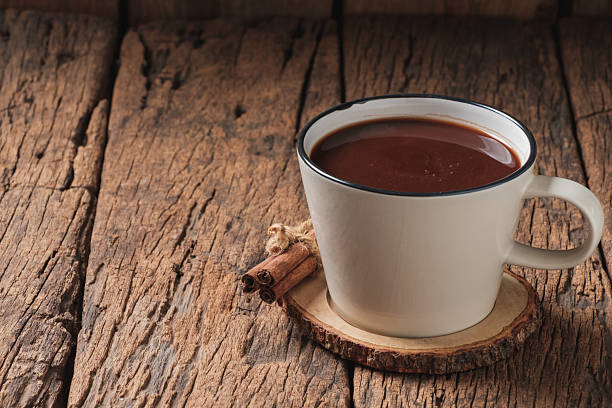 Hot chocolate in white mug with cinnamon sticks on rustic wooden table with copy space.
