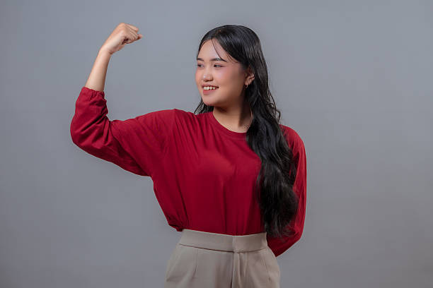 istock Confident young Indonesian woman showing strong arm gesture while smiling proudly. Studio portrait with gray background, expressing empowerment, confidence, and positive attitude. 2240278106