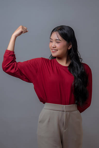 istock Confident young Indonesian woman showing strong arm gesture while smiling proudly. Studio portrait with gray background, expressing empowerment, confidence, and positive attitude. 2240278120
