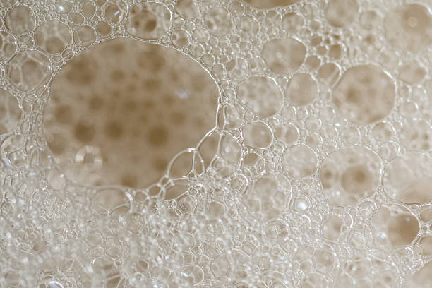 This macro photograph showcases a cluster of soap bubbles, creating an abstract and visually interesting texture. The bubbles are transparent and iridescent, creating a luminous and airy feel against a background of a tan color. Perfect for designs requiring a clean, fresh, or scientific aesthetic.