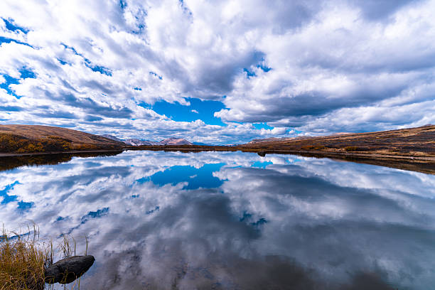 High altitude wide angle view of sky reflecting in calm mirror-like surface of small lake in the alpine zone.
