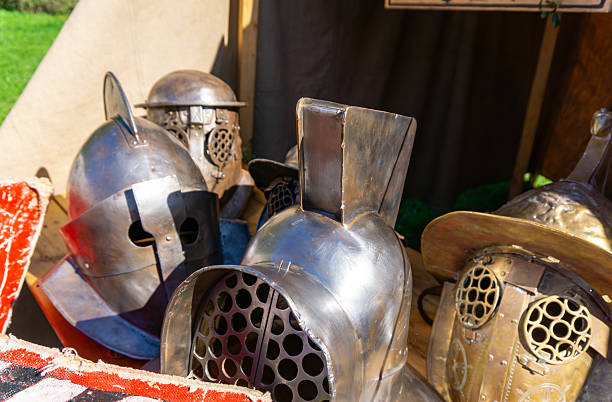 istock Metal Roman gladiator helmets with various visor and guard shapes displayed on a table during a historical reenactment of an ancient Roman military camp. 2240285305
