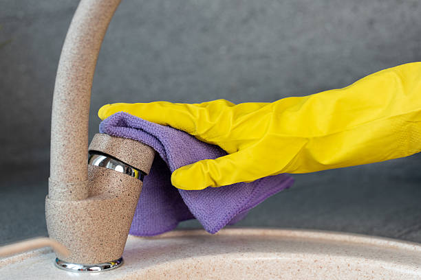 Hands in yellow gloves cleaning a sink with a sponge close up