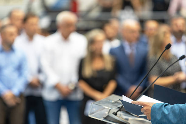 istock Public speaker giving presentation at business or political conference with blurred audience in background, showing leadership, communication, teamwork, and professional public speaking concept in modern corporate environment 2240290138