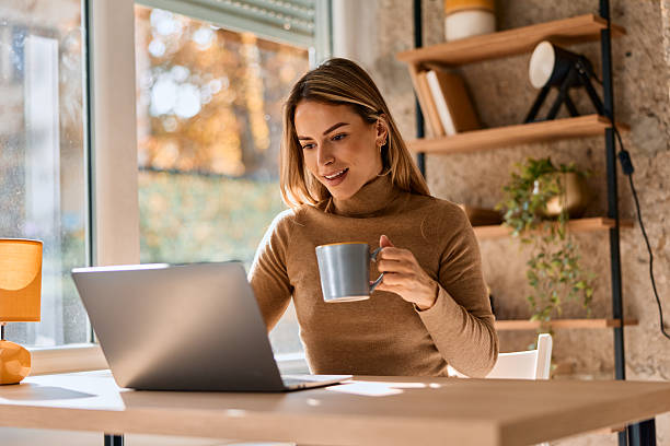 istock Woman working on laptop and drinking coffee at home 2240292902