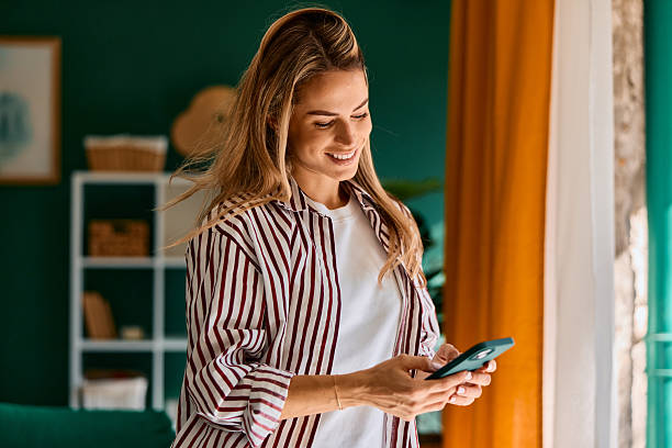 istock Young woman smiling using smartphone at home 2240293524