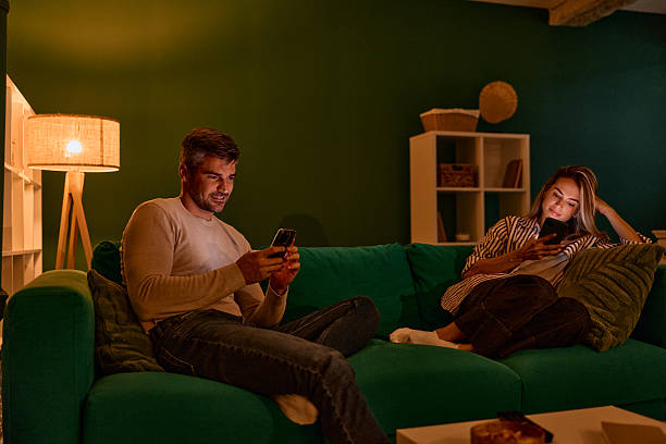 istock Couple relaxing on sofa at night using smartphones 2240294841