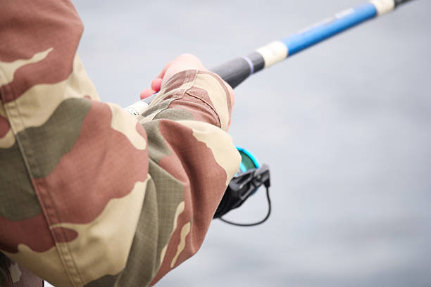 A person wearing a camo jacket is fishing by the water.
