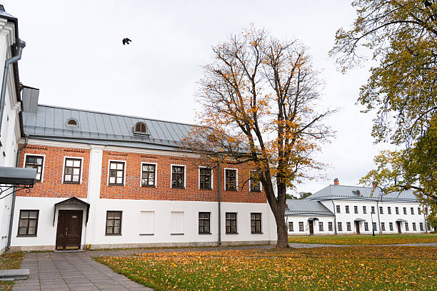 The courtyard of a monastery in autumn, featuring a historic building with brick and white walls, a path, and a lawn covered with yellow fallen leaves